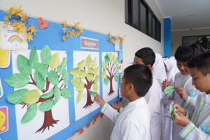 Secara bergantian, siswa menempelkan Daun Harapan mereka ke Pohon Harapan di depan hall 